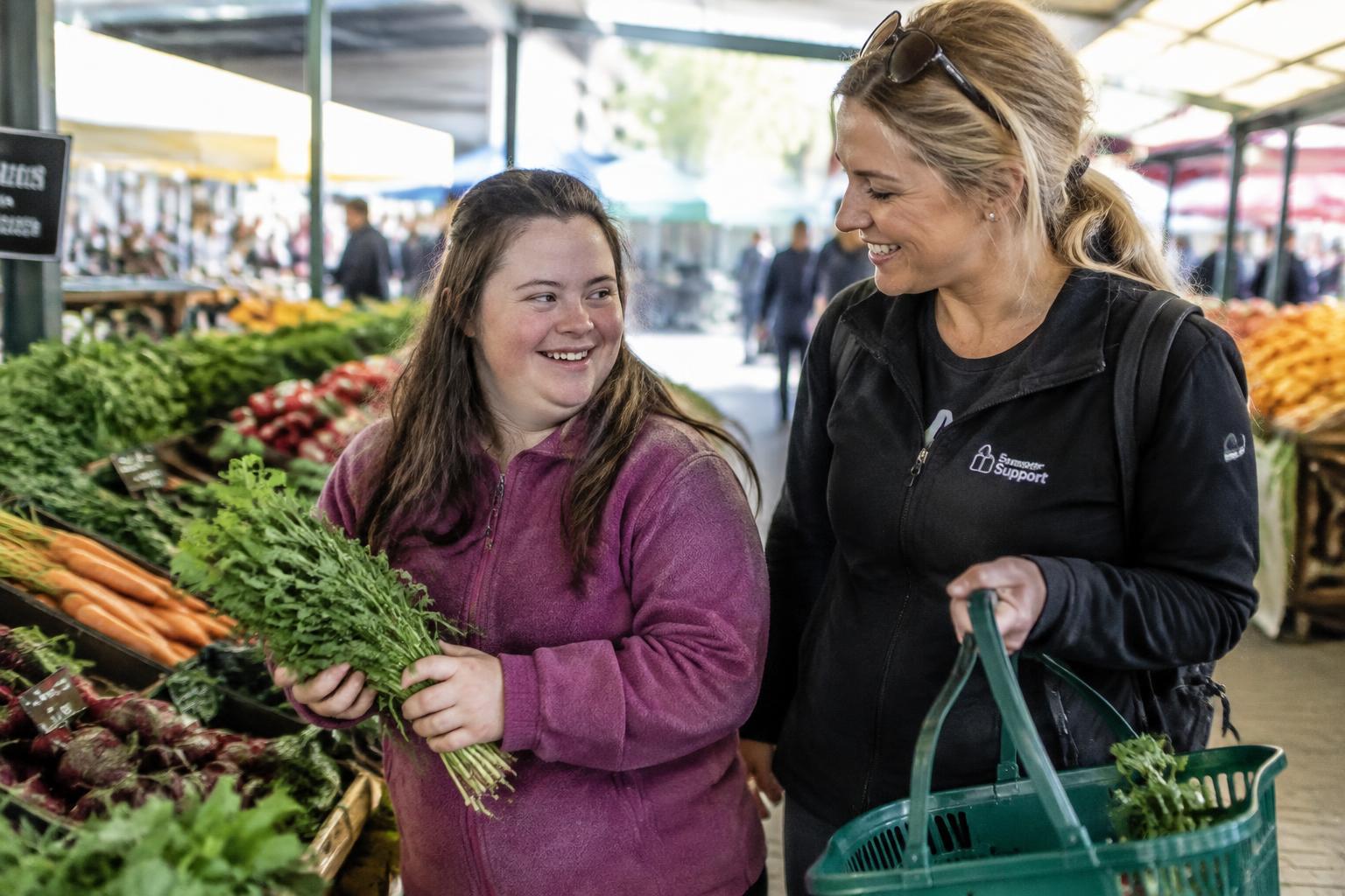 A young woman choosing fresh produce at a market with a support worker